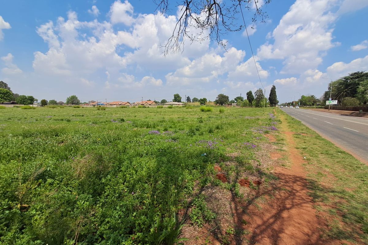 A view of the vacant commercial land parcel adjacent to a paved public road with surrounding residential neighborhood visible in the distance.