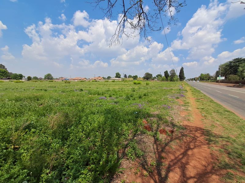 A view of the vacant commercial land parcel adjacent to a paved public road with surrounding residential neighborhood visible in the distance.