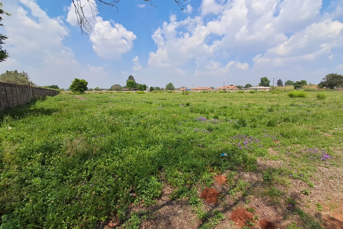 A wide-angle view of a vacant commercial plot featuring natural grass coverage and a precast concrete boundary wall along the side perimeter.