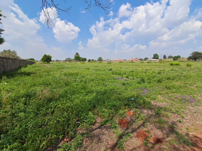 A wide-angle view of a vacant commercial plot featuring natural grass coverage and a precast concrete boundary wall along the side perimeter.