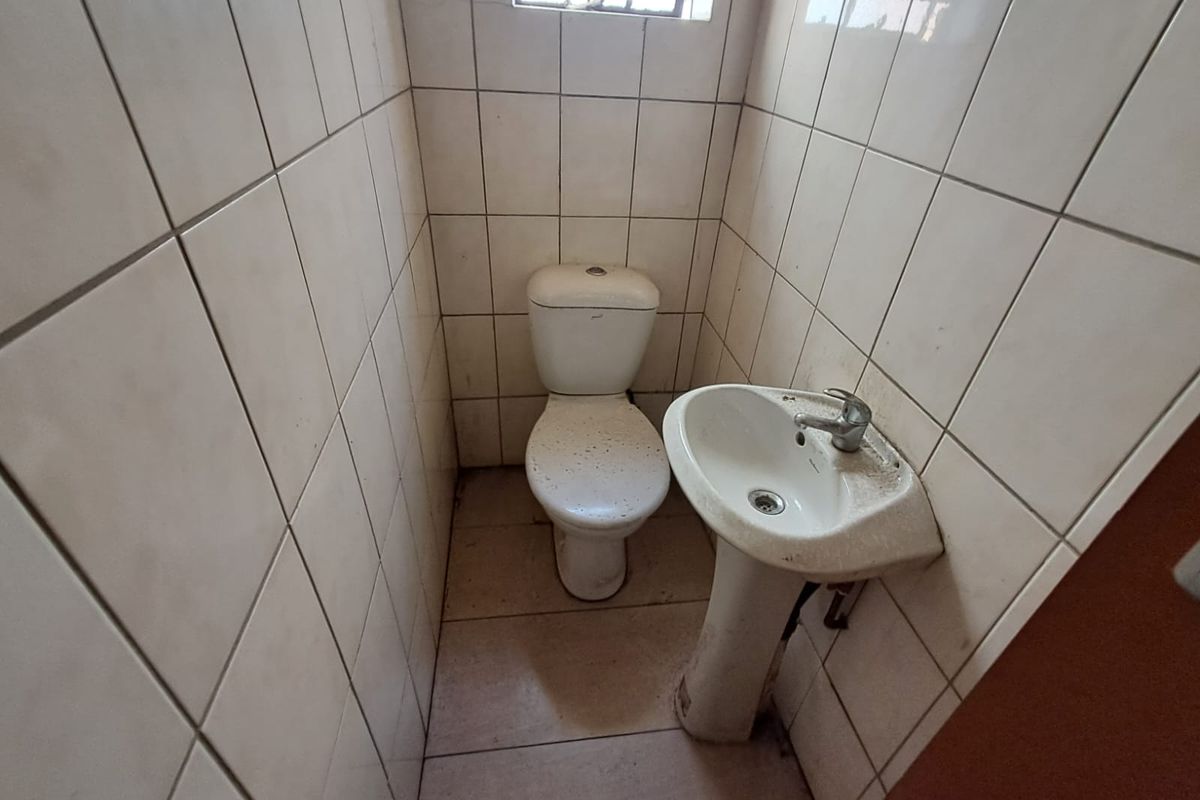A small, functional industrial bathroom featuring a pedestal basin and toilet with full-height wall tiling.