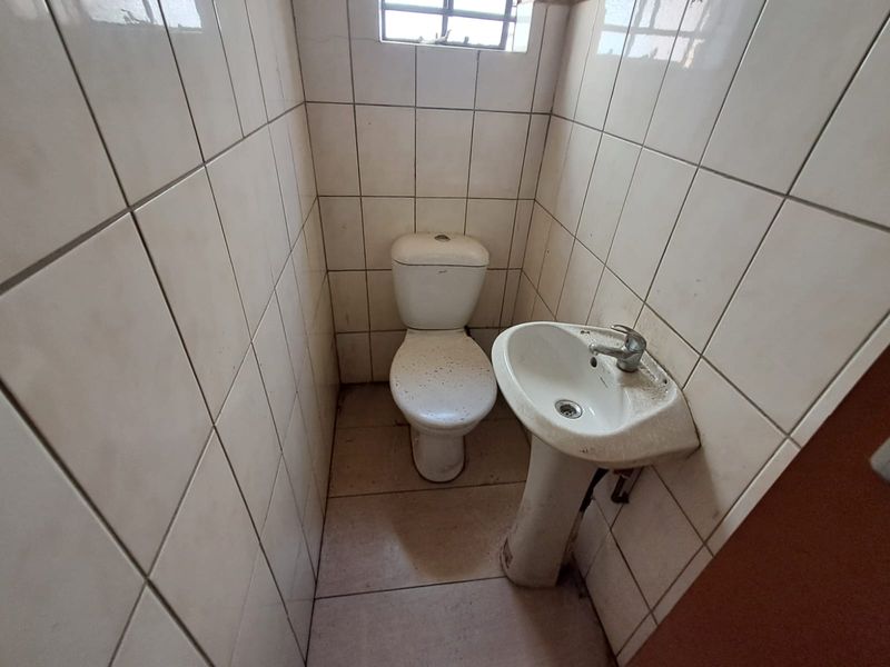 A small, functional industrial bathroom featuring a pedestal basin and toilet with full-height wall tiling.