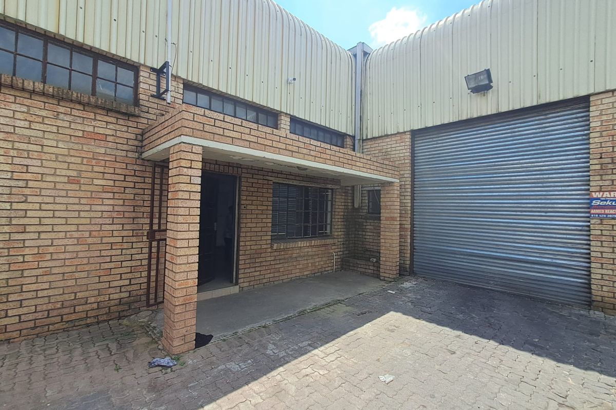 Industrial property exterior featuring a brick facade, a large roller shutter door, and a covered entrance area with paved driveway access.