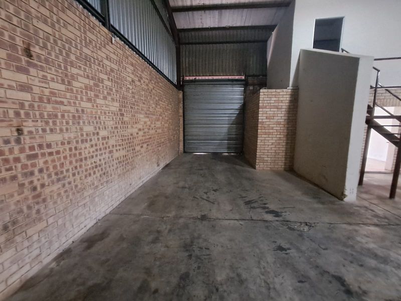 Spacious industrial garage area featuring exposed brick walls, concrete flooring, and a secure roller shutter door, suitable for storage or workshop use.