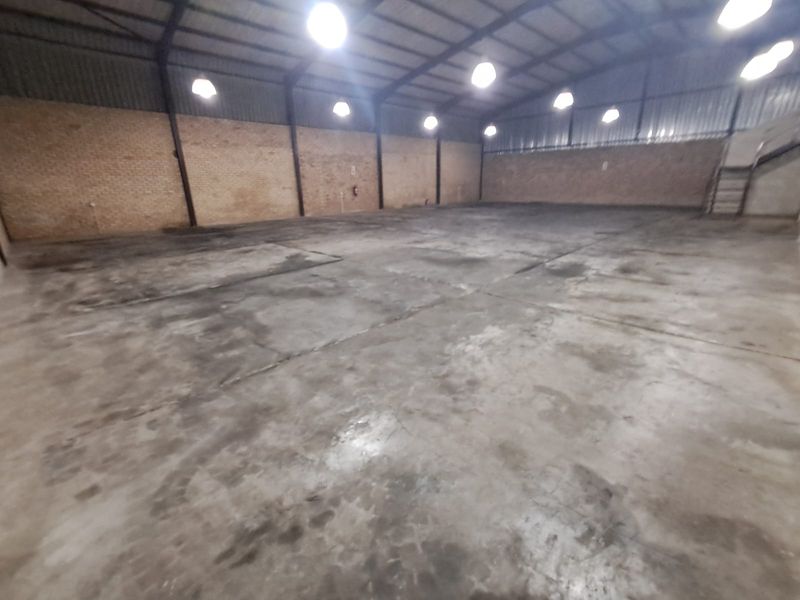 Spacious industrial warehouse unit featuring exposed brick walls, durable concrete flooring, and high-clearance steel portal frame construction with overhead industrial lighting.