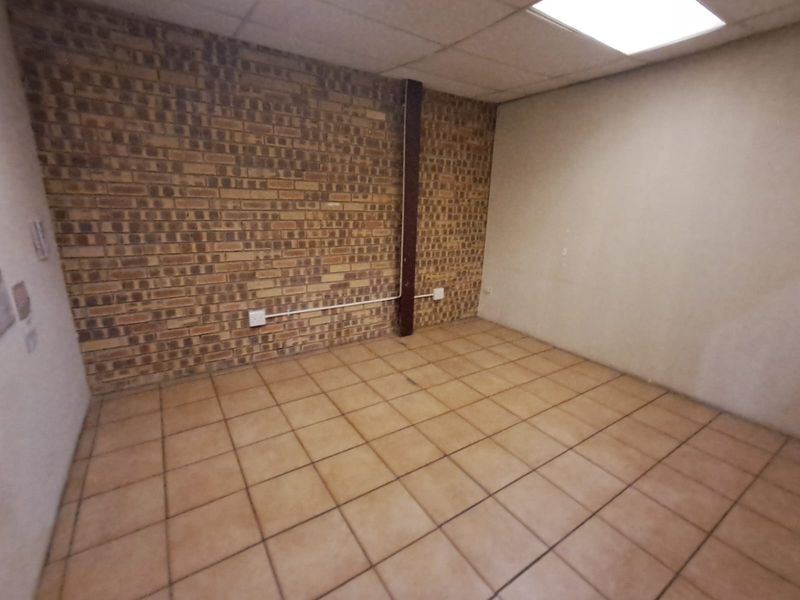 An empty industrial-style office space featuring exposed brickwork, tiled flooring, and a suspended ceiling with recessed lighting.