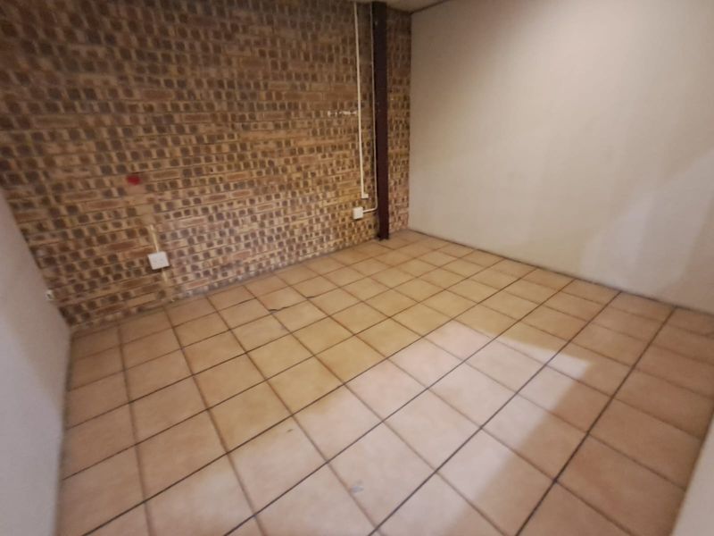 An empty utility space featuring exposed brickwork, ceramic tiled flooring, and a structural steel column, suitable for various industrial or storage applications.
