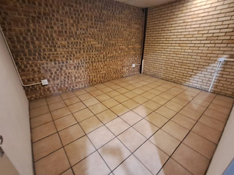 An empty utility space featuring exposed brick walls and ceramic tile flooring with surface-mounted electrical infrastructure.