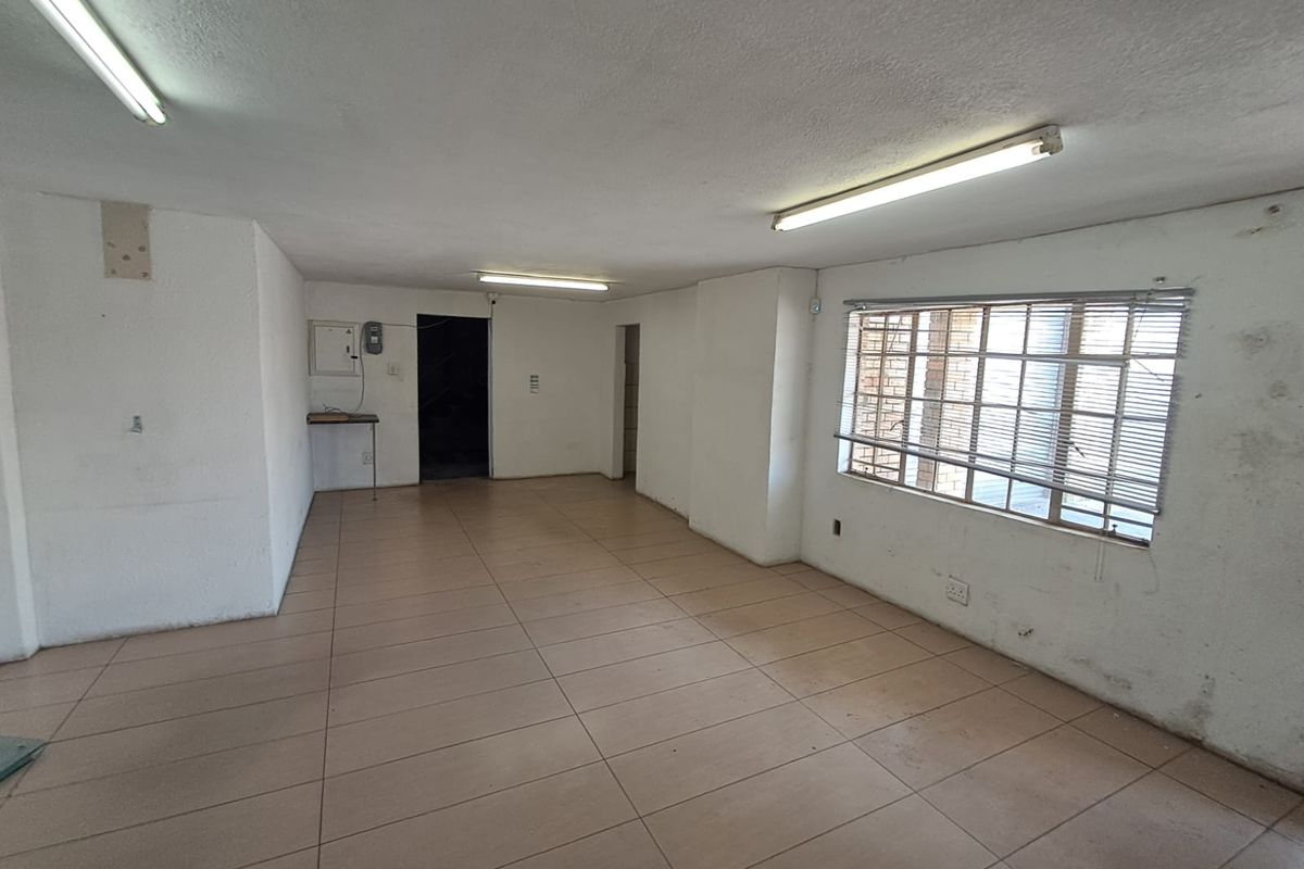An empty, open-plan industrial space featuring tiled flooring, fluorescent lighting, and security-barred windows, suitable for a variety of commercial or workshop uses.