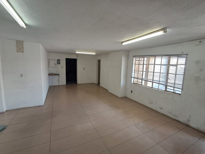 An empty, open-plan industrial space featuring tiled flooring, fluorescent lighting, and security-barred windows, suitable for a variety of commercial or workshop uses.