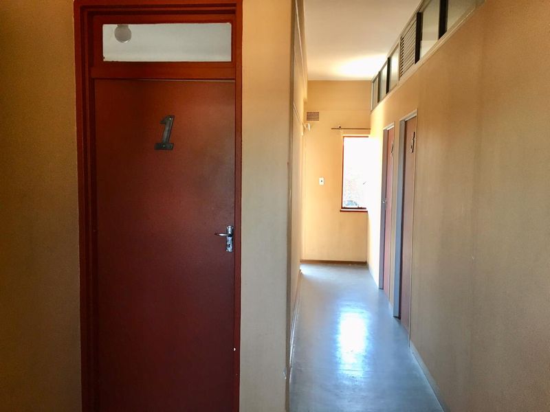 A functional apartment hallway featuring multiple internal doors with transom windows and a small window at the end providing natural light.