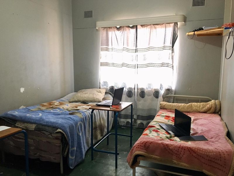 A shared bedroom featuring basic finishes, ventilation grilles, and a curtain rail. The room requires cosmetic updates to improve its overall condition.