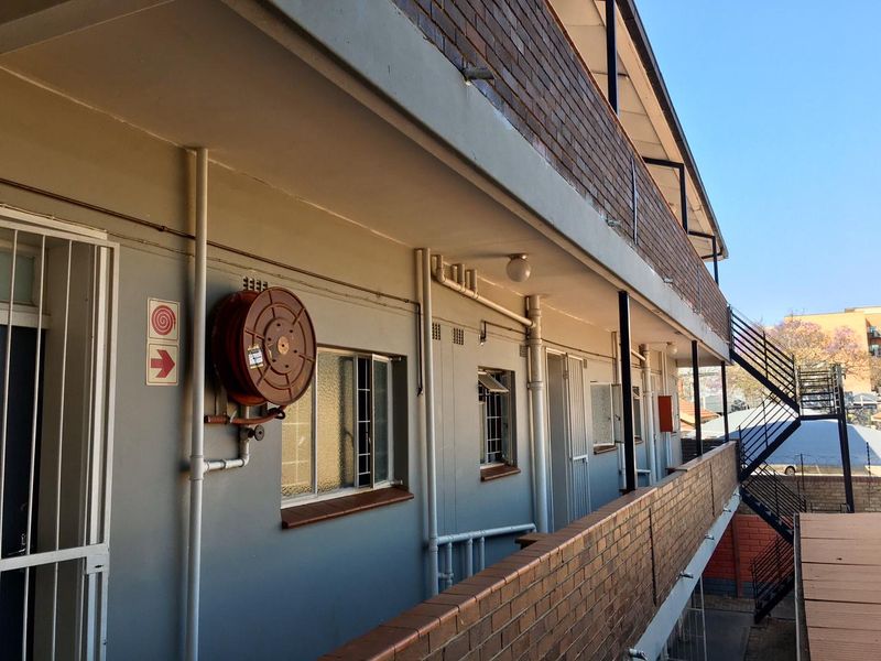 Exterior view of an apartment building walkway featuring brick facade, metal staircase, and installed fire safety equipment.