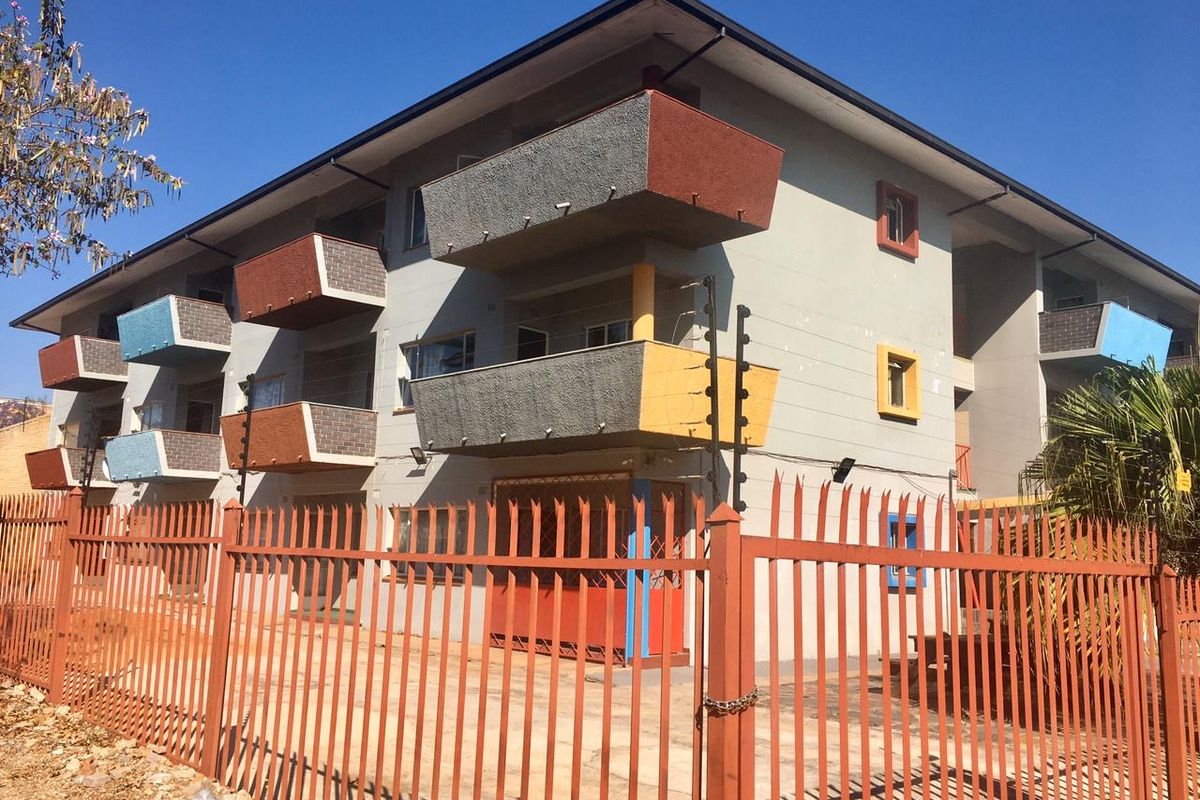 Exterior view of a multi-story apartment building featuring private balconies, security fencing, and a gated entrance.