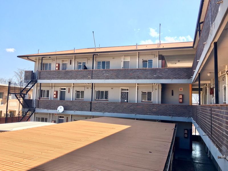Exterior view of a multi-story apartment complex featuring brick facade, metal walkways, and external staircases under a clear sky.