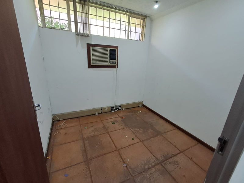 A vacant office space featuring tiled flooring, a window-mounted air conditioning unit, and high-level clerestory windows providing natural light.
