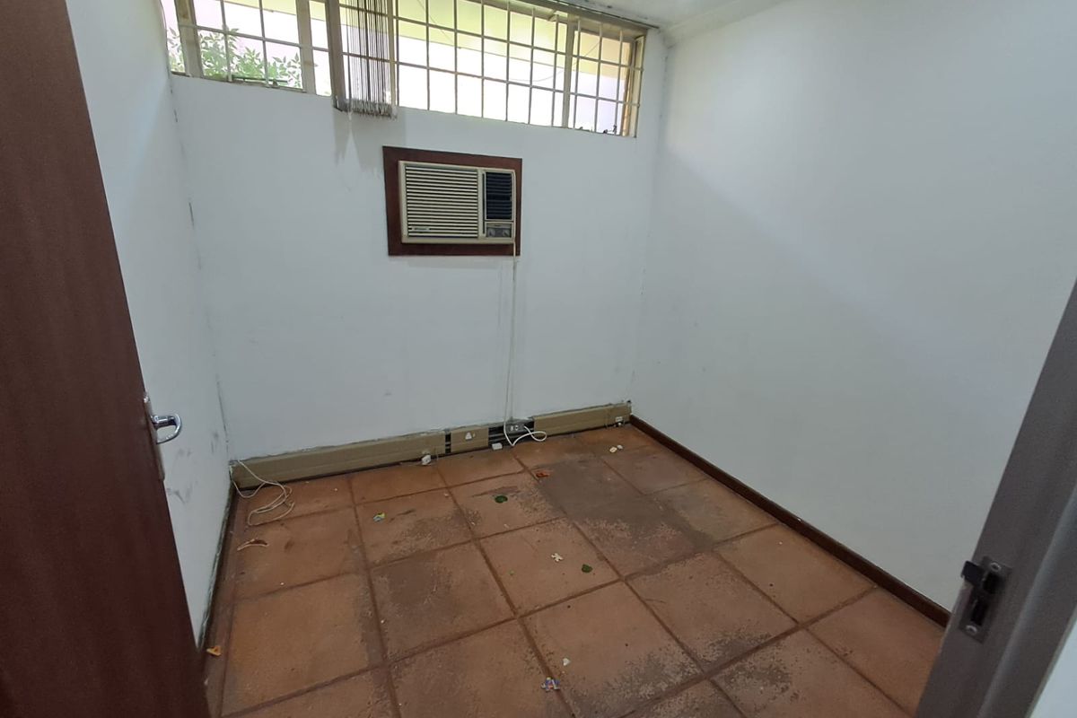 A vacant office space featuring tiled flooring, a window-mounted air conditioning unit, and high-level clerestory windows providing natural light.