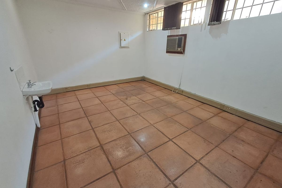An empty office space featuring tiled flooring, a wall-mounted basin, and a window-mounted air conditioning unit.