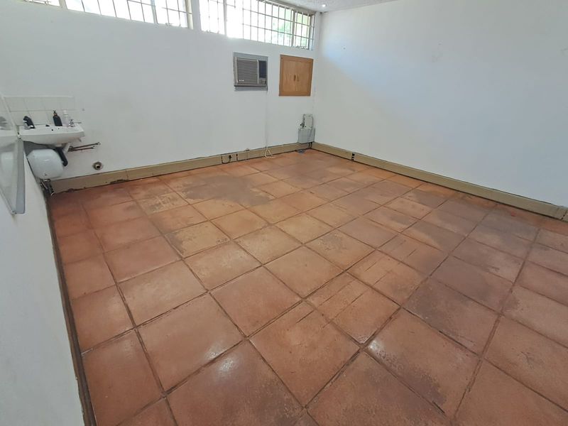 An empty office space featuring terracotta tiled flooring, a wall-mounted basin, and high-level clerestory windows, providing a functional blank canvas for professional use.
