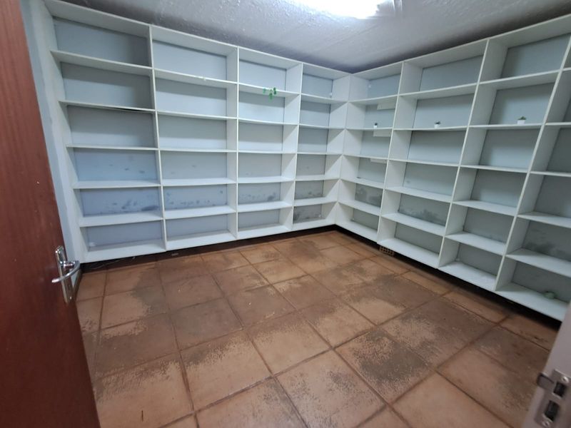 An empty office space featuring extensive built-in wall shelving and tiled flooring, suitable for storage or a dedicated workspace.