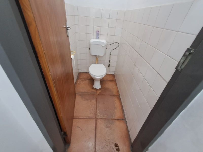 A small, functional office restroom featuring a standard toilet, white wall tiling, and terracotta-style floor tiles.