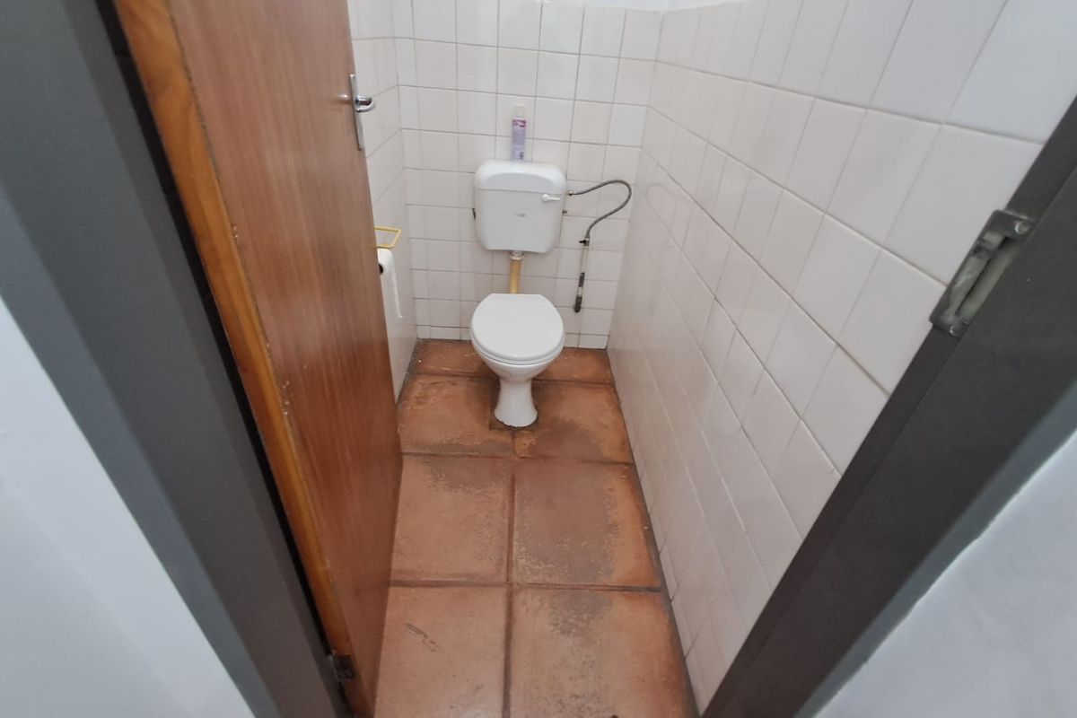 A small, functional office restroom featuring a standard toilet, white wall tiling, and terracotta-style floor tiles.