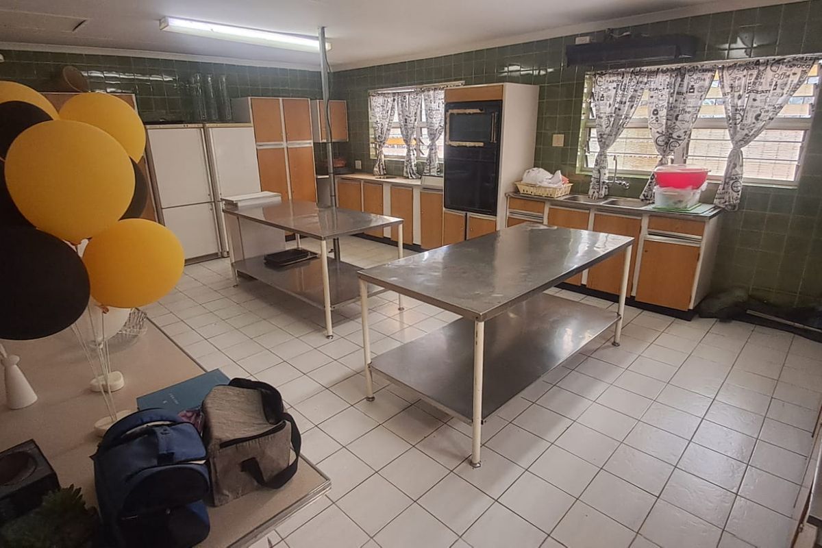 A functional commercial-style kitchen featuring stainless steel prep tables, built-in cabinetry, and tiled surfaces, suitable for high-volume guest house catering.