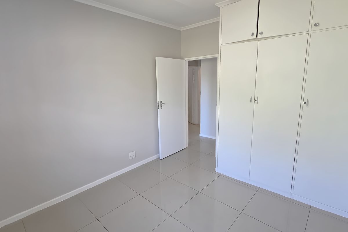 A bright, empty bedroom featuring neutral wall tones, large format floor tiles, and ample built-in cupboard storage.
