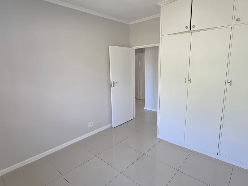 A bright, empty bedroom featuring neutral wall tones, large format floor tiles, and ample built-in cupboard storage.