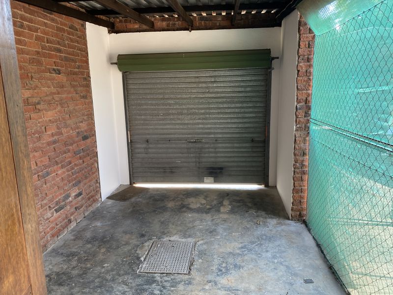 A functional single garage space featuring exposed brick walls, a concrete floor, and a secure roller shutter door.