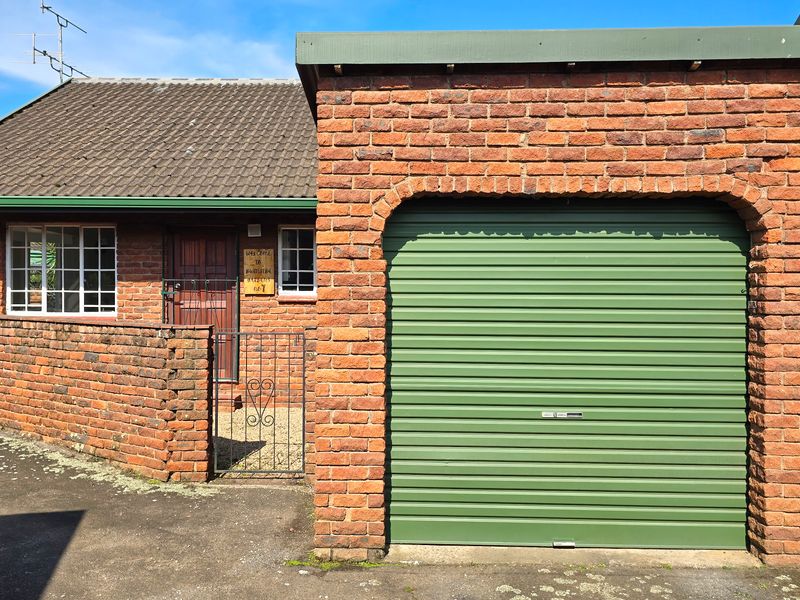 Front exterior view of a brick townhouse featuring a roller garage door, tiled roof, and a gated entrance with security bars.