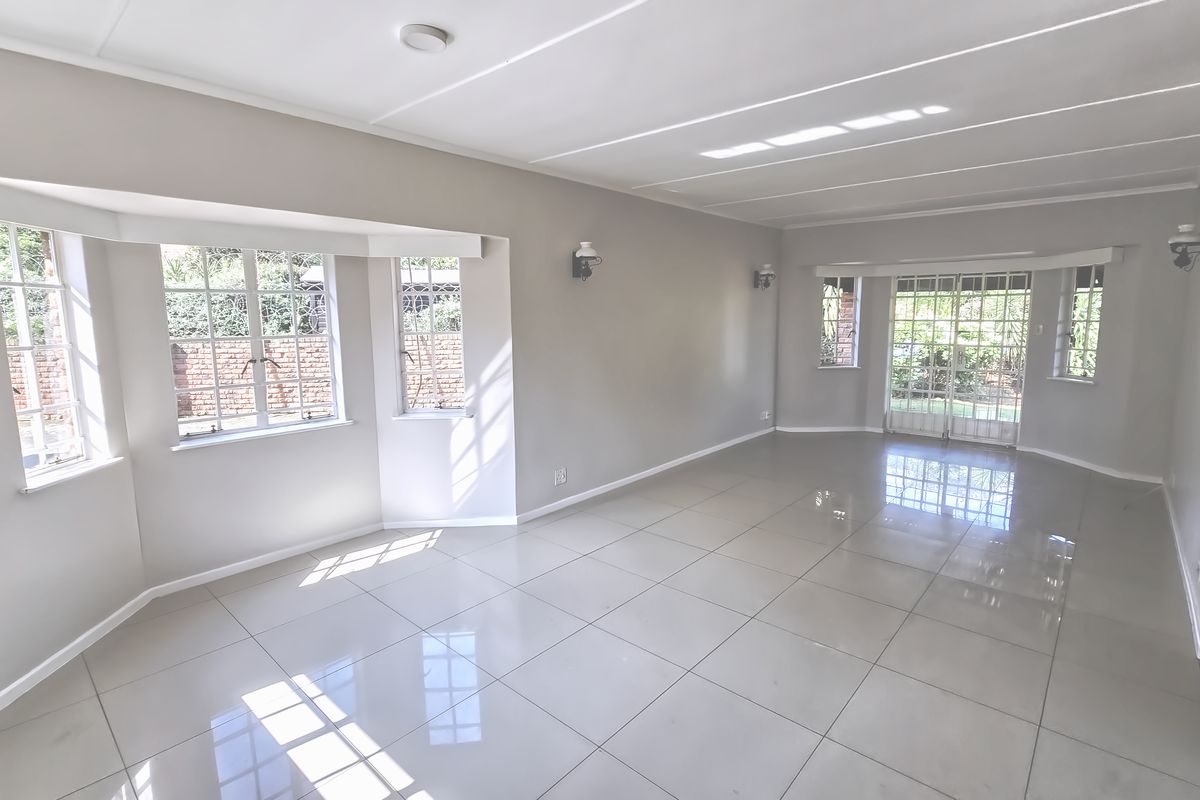 Spacious, light-filled living area featuring neutral walls, polished tile flooring, and large bay windows with access to the garden through french doors.
