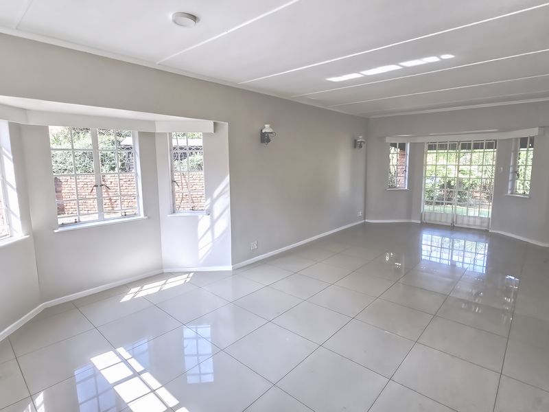 Spacious, light-filled living area featuring neutral walls, polished tile flooring, and large bay windows with access to the garden through french doors.