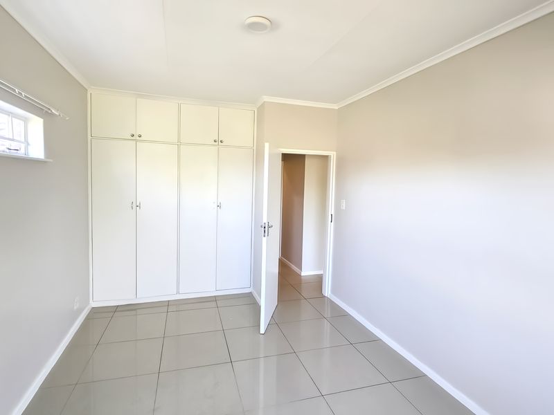 A bright, empty bedroom featuring neutral tiled flooring, built-in cupboards with overhead storage, and a clean, minimalist aesthetic.