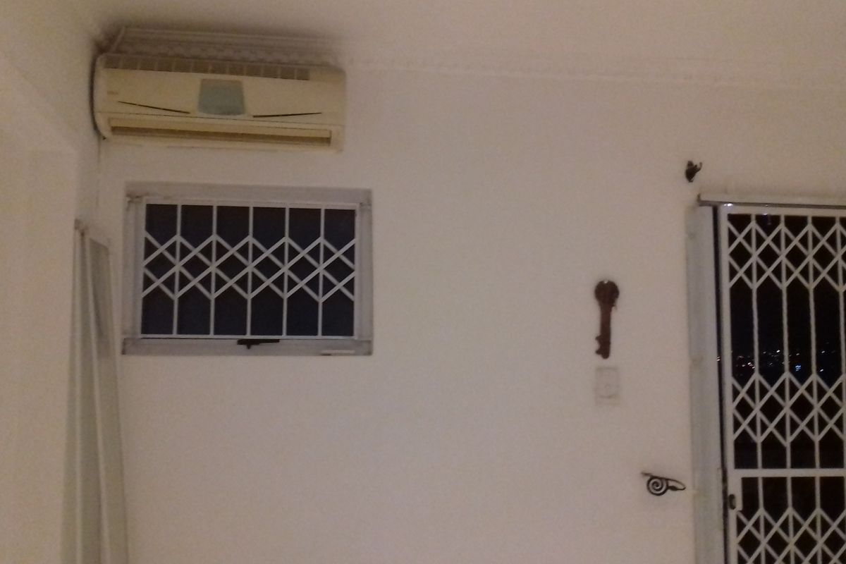 Interior living space featuring a wall-mounted air conditioning unit, security bars on the window, and a sliding door with a security gate.