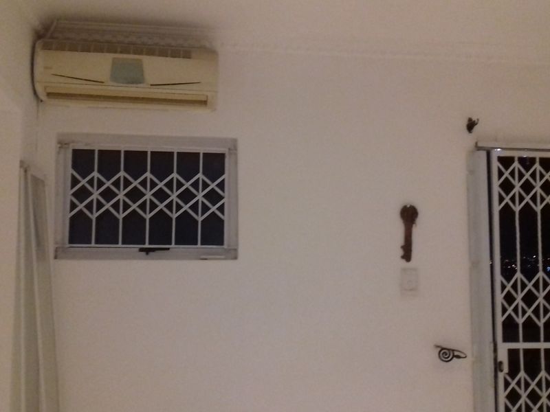 Interior living space featuring a wall-mounted air conditioning unit, security bars on the window, and a sliding door with a security gate.
