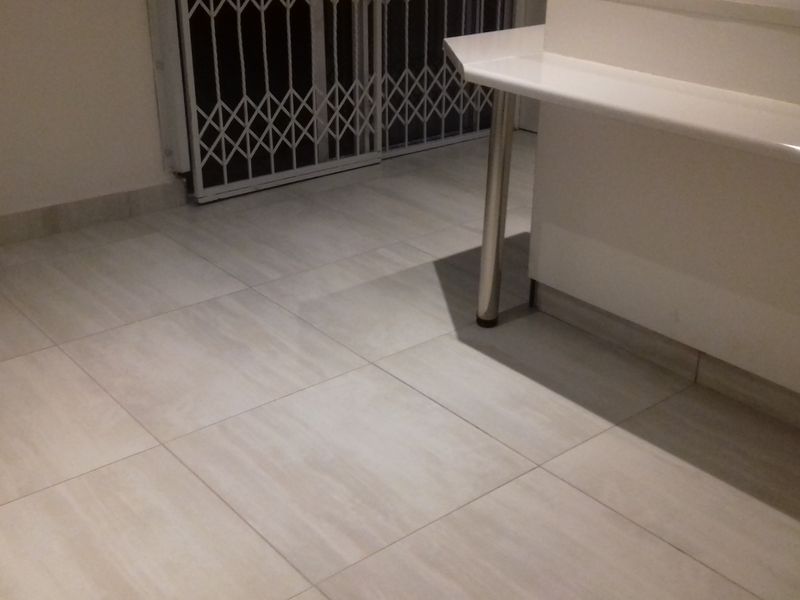 A clean, empty kitchen area featuring neutral tiled flooring and a built-in breakfast bar with a metal support leg.