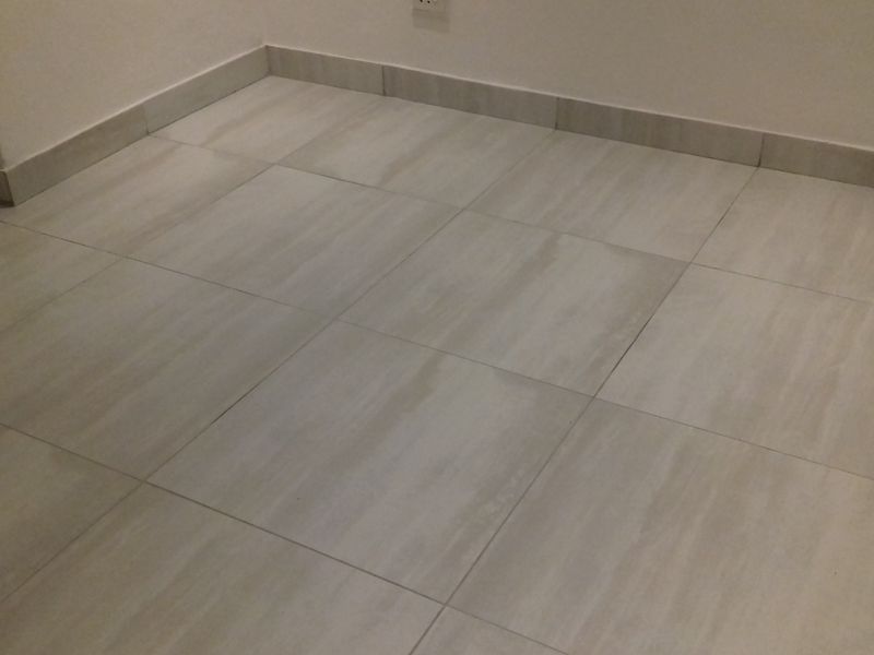 A close-up view of neutral-toned ceramic floor tiles with matching skirting boards in an empty room.