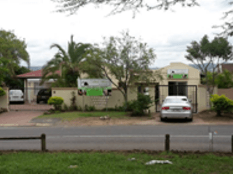 Front elevation of the cottage property featuring a boundary wall, security gate, and paved driveway with a carport.