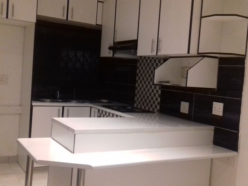 A functional kitchen featuring white cabinetry, contrasting black and white tiled backsplash, integrated breakfast bar, and built-in sink and extractor fan.