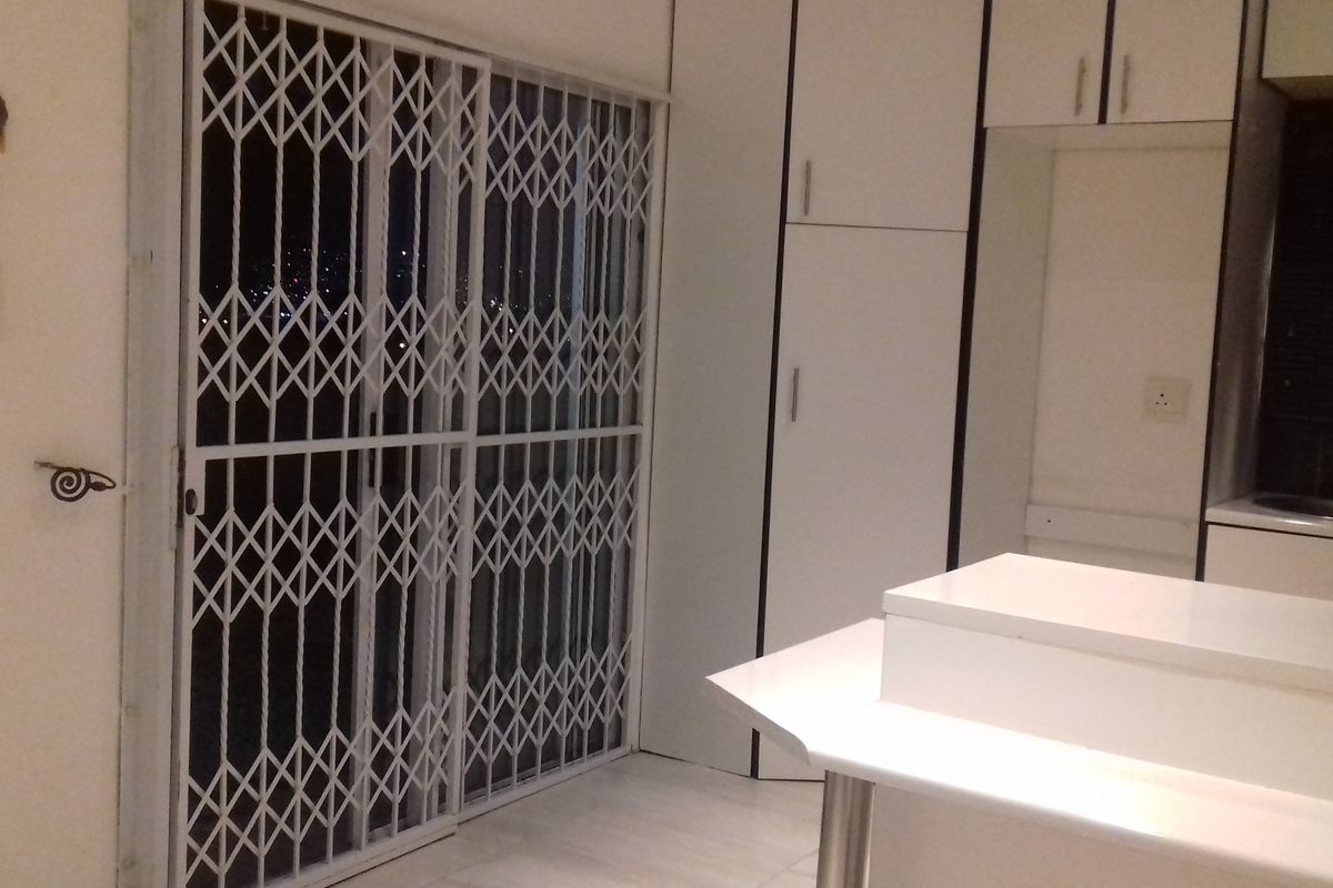A functional kitchen area featuring built-in white cabinetry, a countertop, and a sliding door secured with a metal security gate.
