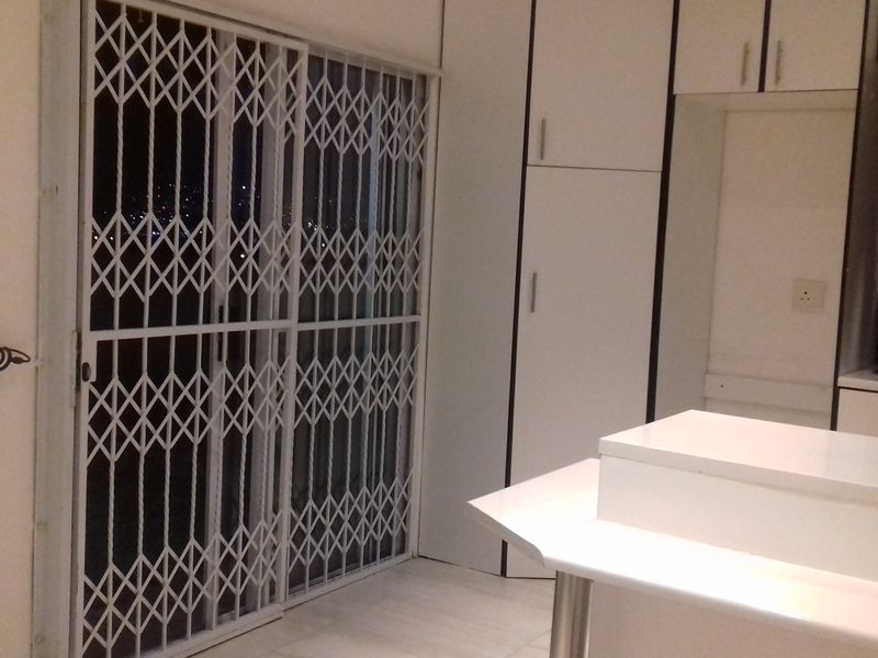 A functional kitchen area featuring built-in white cabinetry, a countertop, and a sliding door secured with a metal security gate.