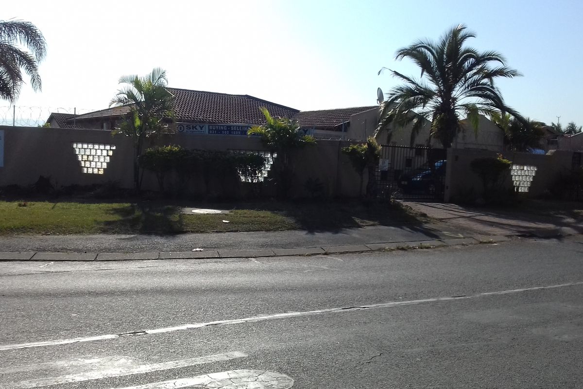 Street view of the property featuring a perimeter wall with glass block accents, a tiled roof, and a gated driveway entrance.