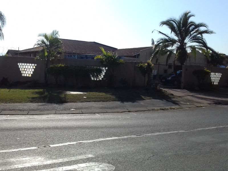Street view of the property featuring a perimeter wall with glass block accents, a tiled roof, and a gated driveway entrance.