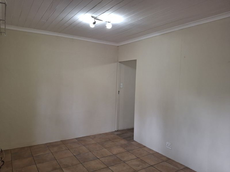 An empty living room featuring tiled flooring, a white timber tongue and groove ceiling, and neutral wall finishes.