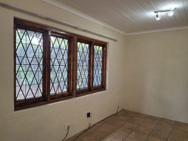A bright, empty living room featuring classic timber-framed leaded glass windows, tiled flooring, and a white tongue-and-groove ceiling with track lighting.
