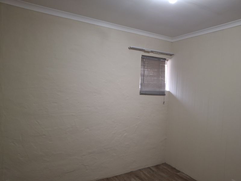 An empty bedroom featuring neutral painted walls, laminate flooring, and a window fitted with venetian blinds.