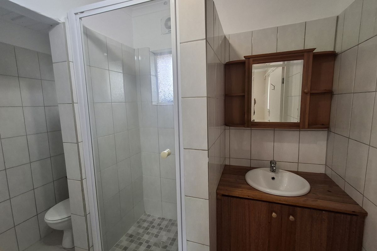 A functional bathroom featuring a shower enclosure, vanity cabinet with basin, wall mirror, and toilet, finished with neutral wall tiling.