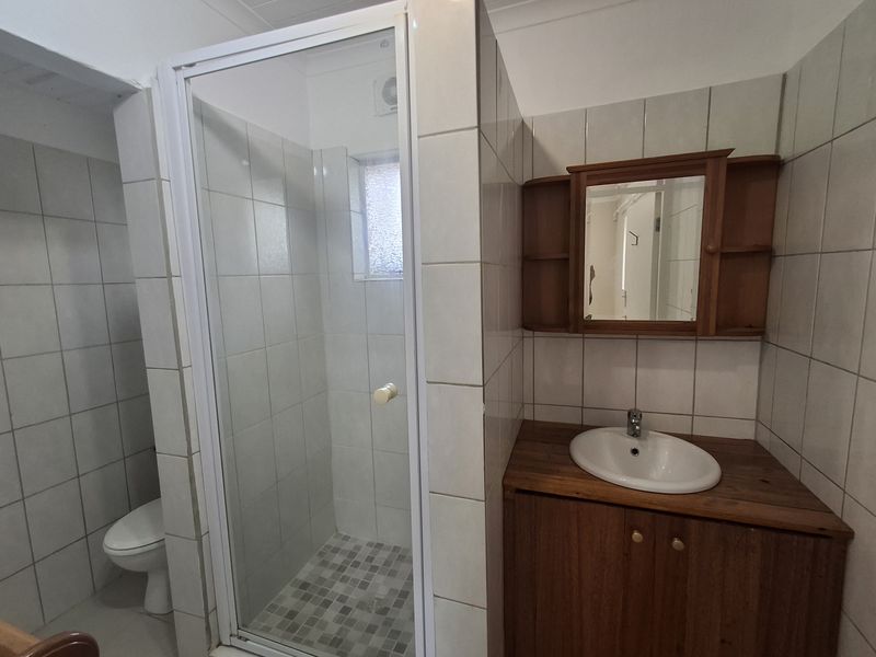 A functional bathroom featuring a shower enclosure, vanity cabinet with basin, wall mirror, and toilet, finished with neutral wall tiling.