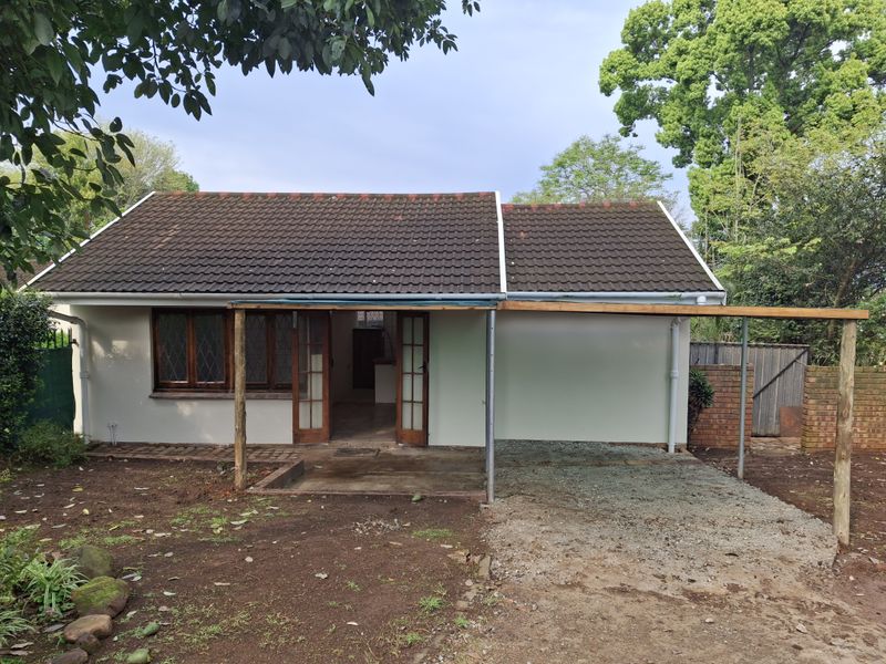 Rear view of the cottage featuring a tiled roof, timber-framed windows and doors, a covered patio area, and an attached carport structure.